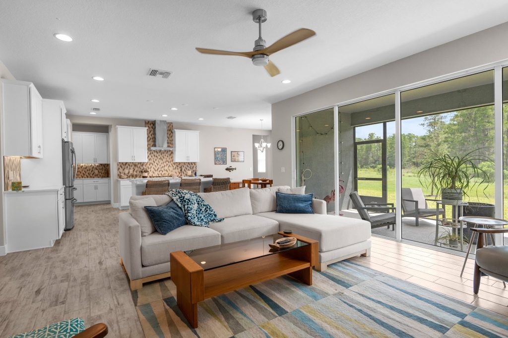 Open-concept living room with staged furnishings, sectional sofa, area rug, wood coffee table, and large sliding glass doors overlooking backyard